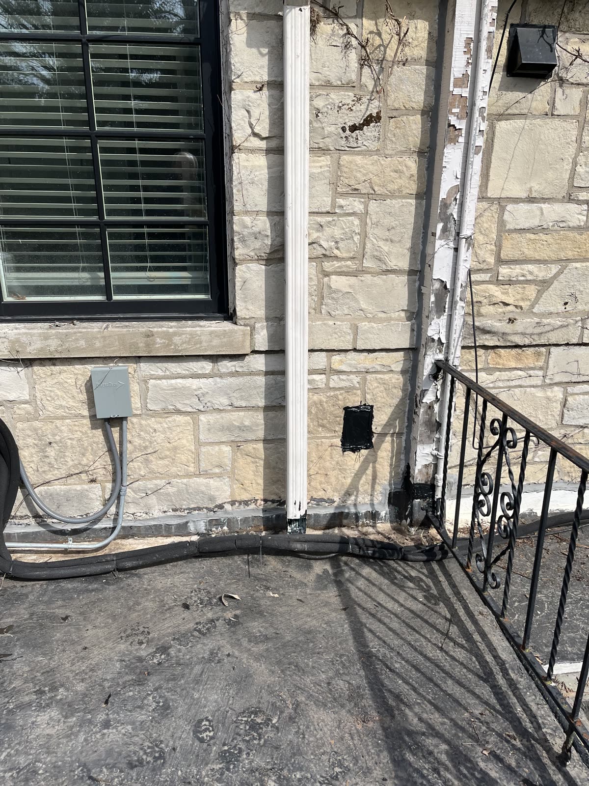 Downspout with no elbow and loose electrical conduit on Winnetka stone home before repair