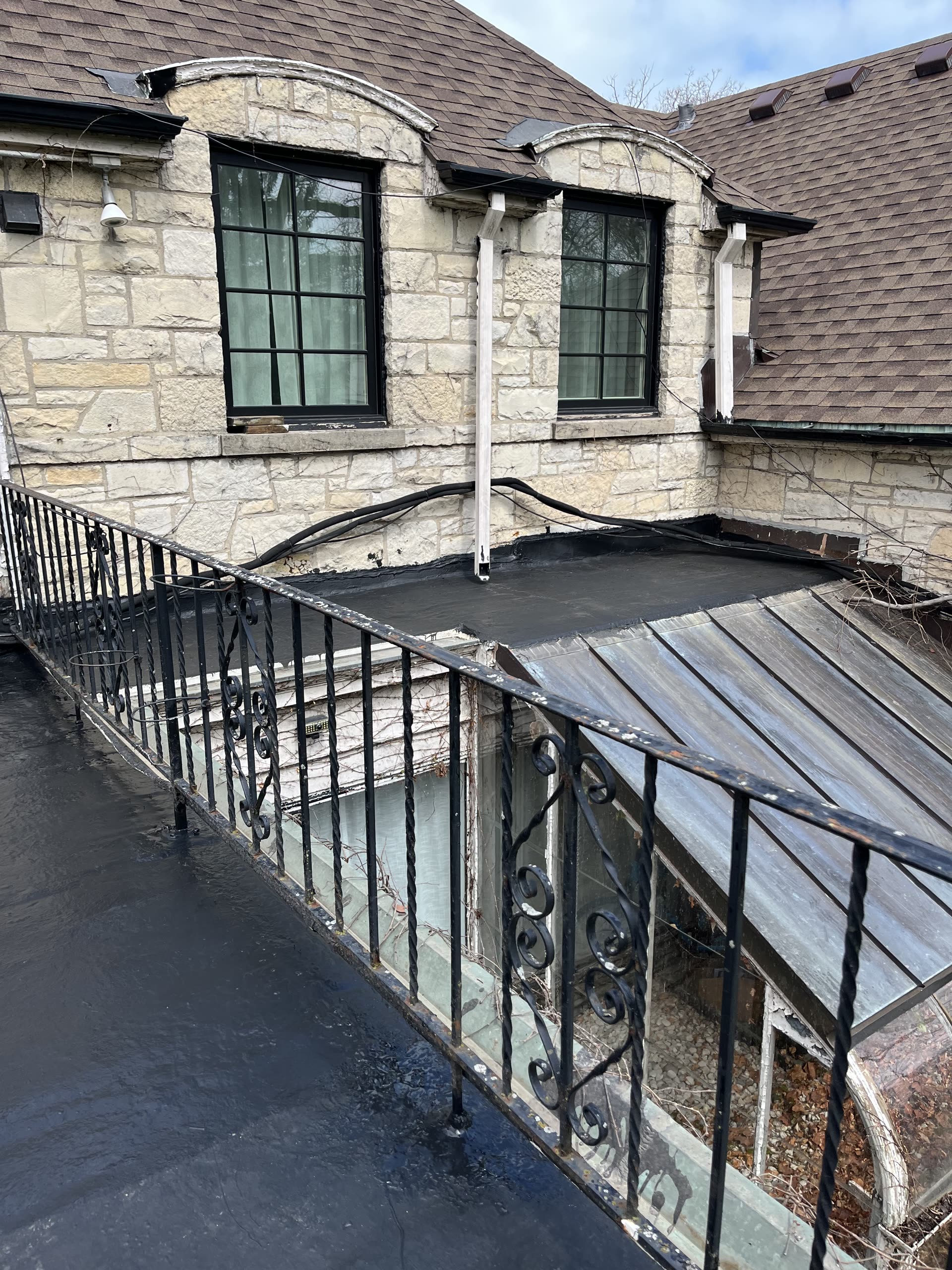 Stone home exterior with newly coated balcony roof and iron railing, Winnetka IL